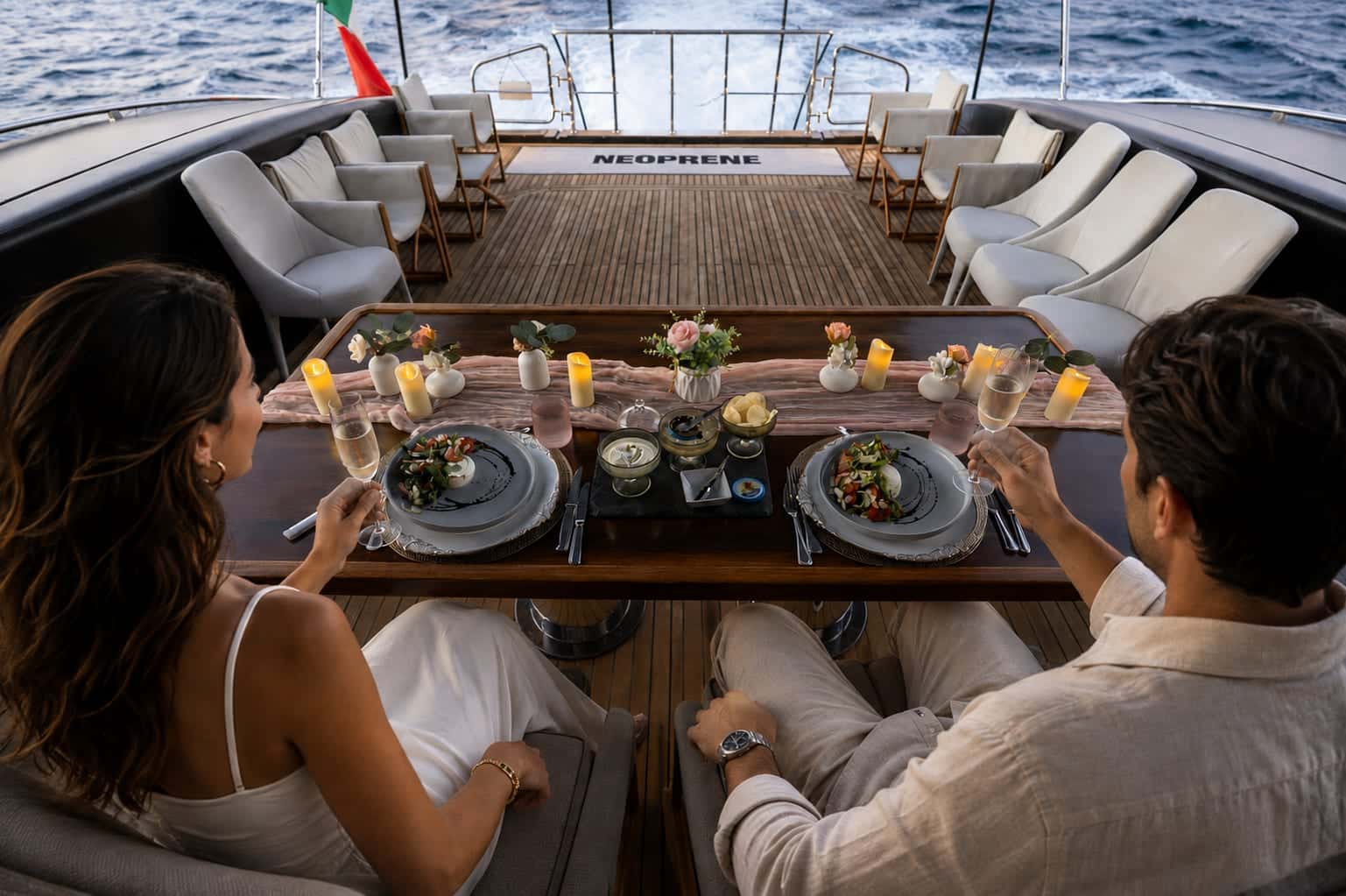 Two guests at a candlelit table on Neoprene's aft deck, a plated salad before each, glasses of champagne in hand