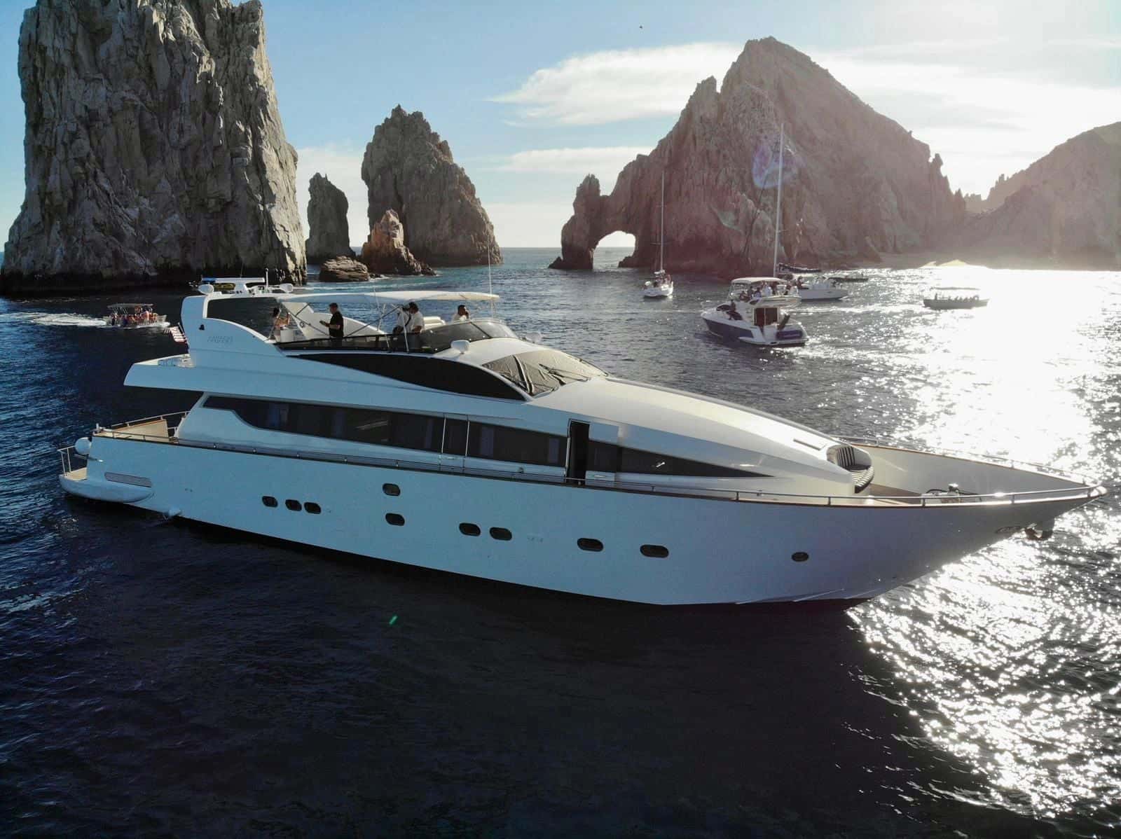 The yacht anchored below the arch and rocks of Land's End, sun low behind