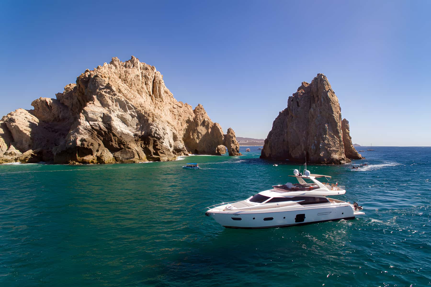 Yacht at anchor in green water in front of two rock formations