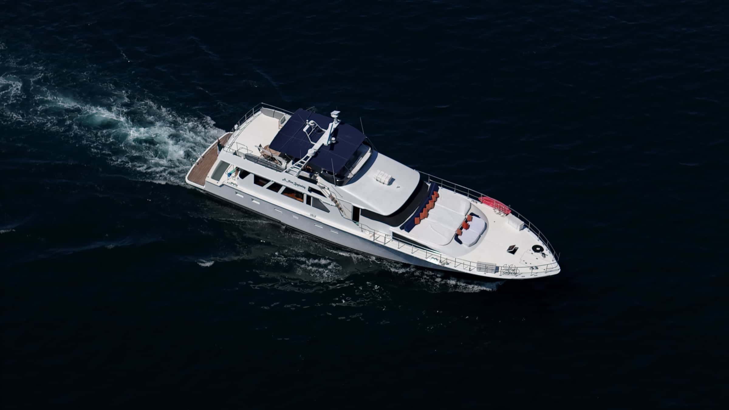 The yacht underway on dark blue water, seen from above, a wake trailing astern