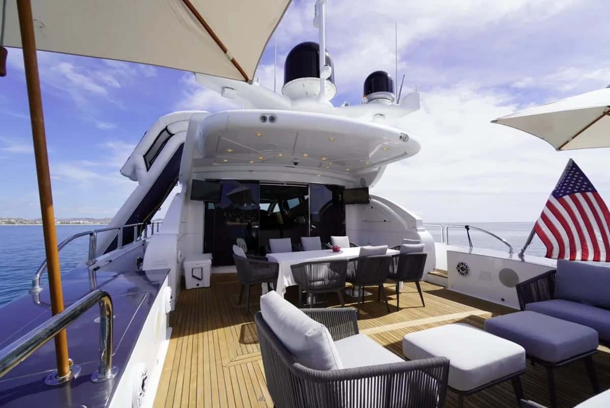 Aft deck with a set dining table, grey lounge chairs and two umbrellas under the flybridge overhang