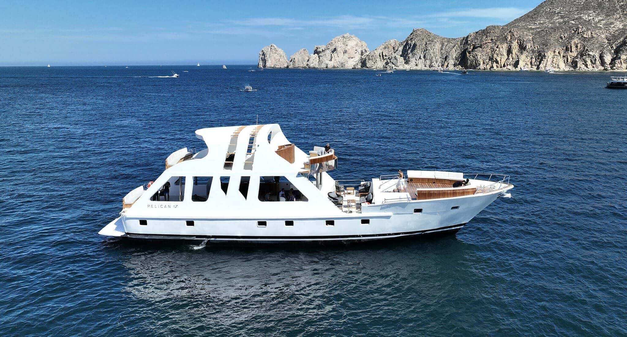 White three-deck yacht on deep blue water with the Land's End cliffs behind