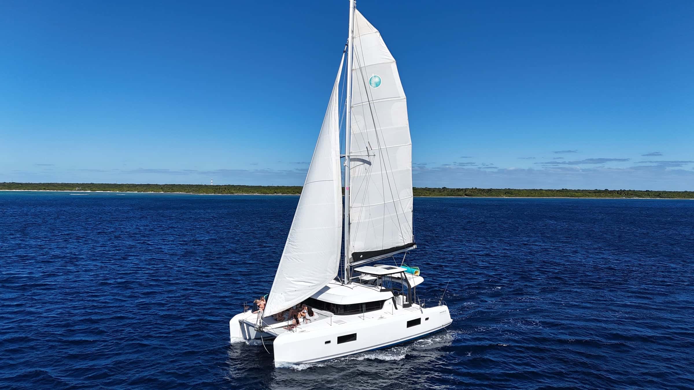 White Lagoon 42 catamaran under main and jib on deep blue water, a low green coast behind