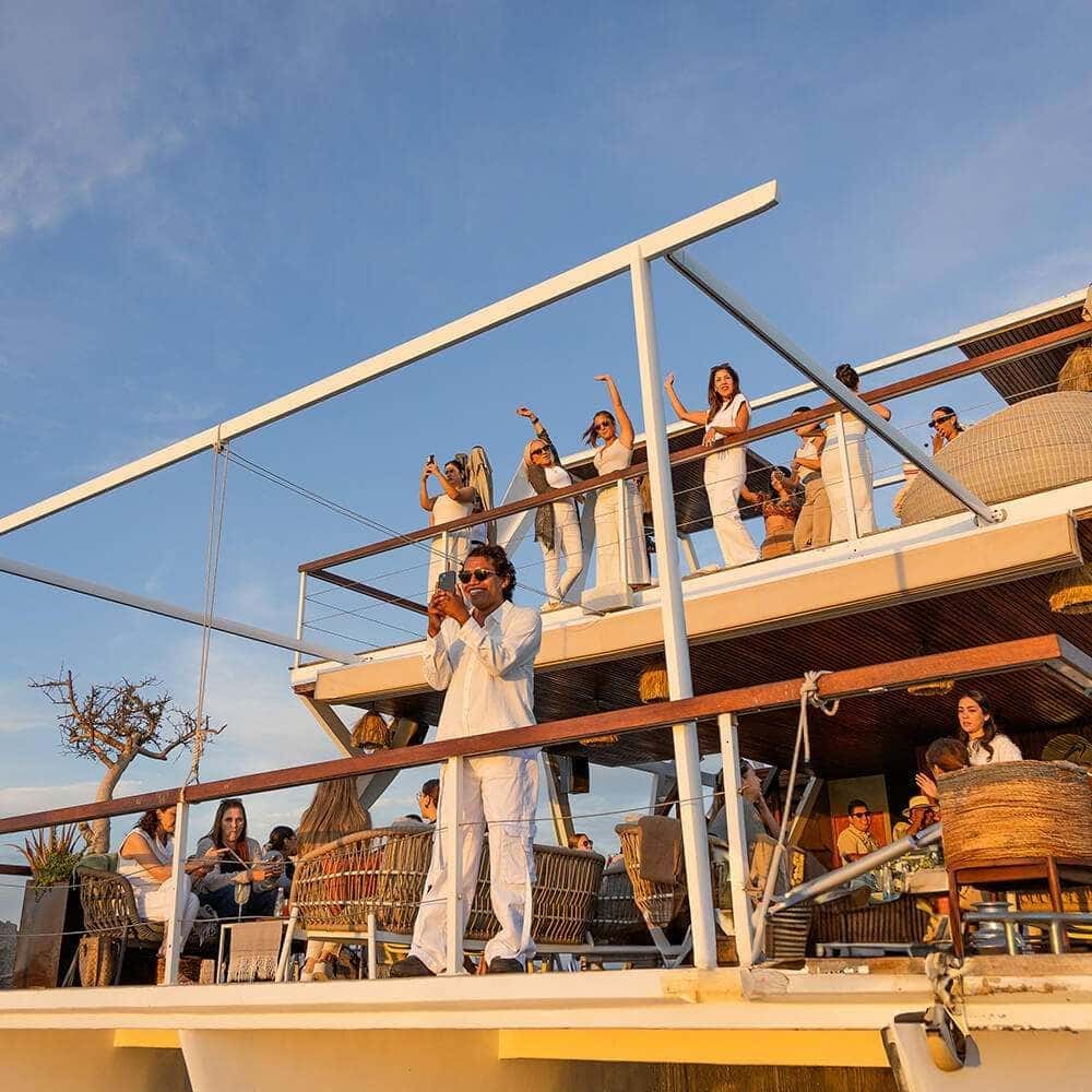 Guests in white waving from the upper deck rail in late sun, the shaded lower deck below