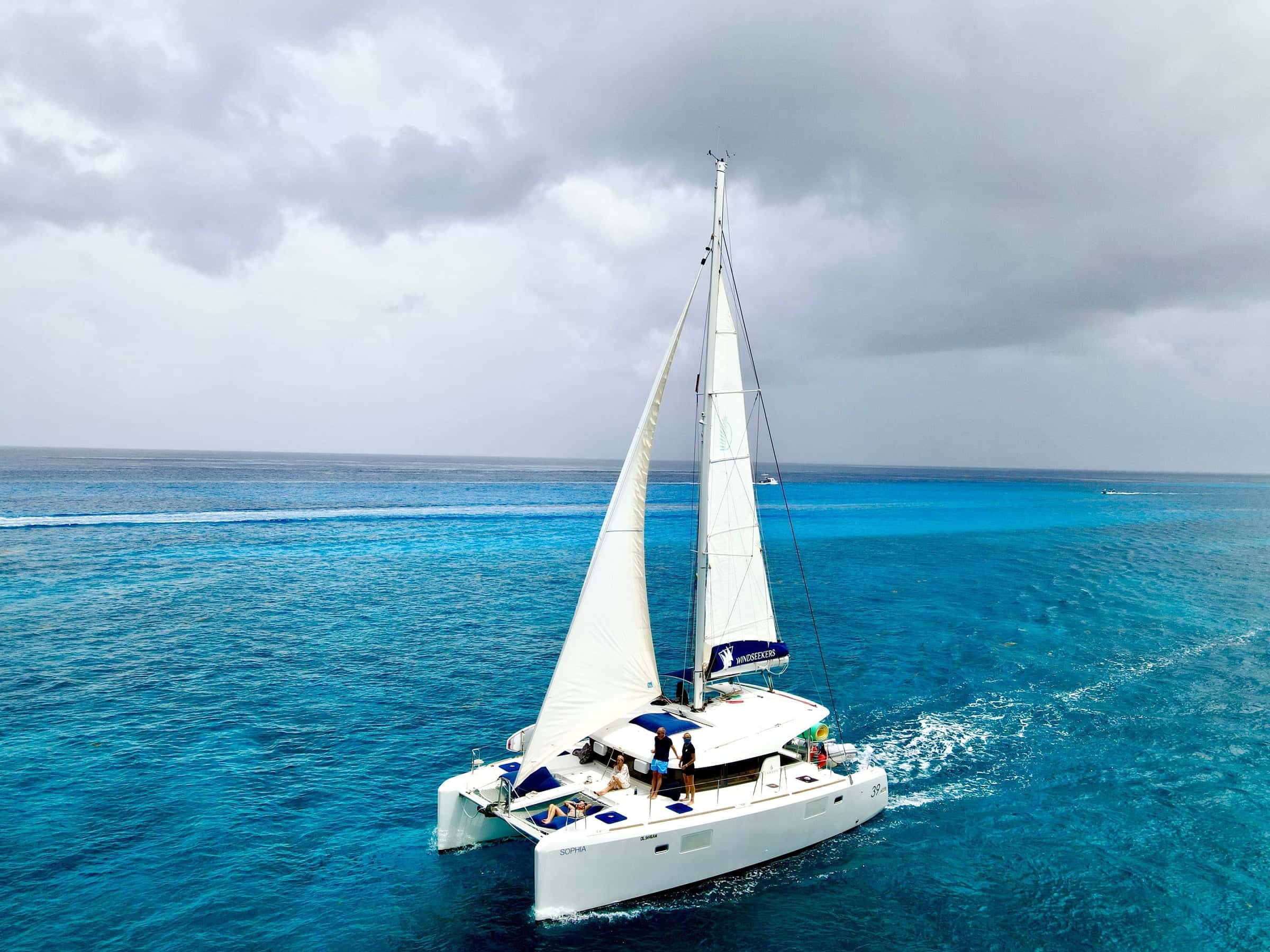 Catamaran under full sail from above, a white wake across deep blue water