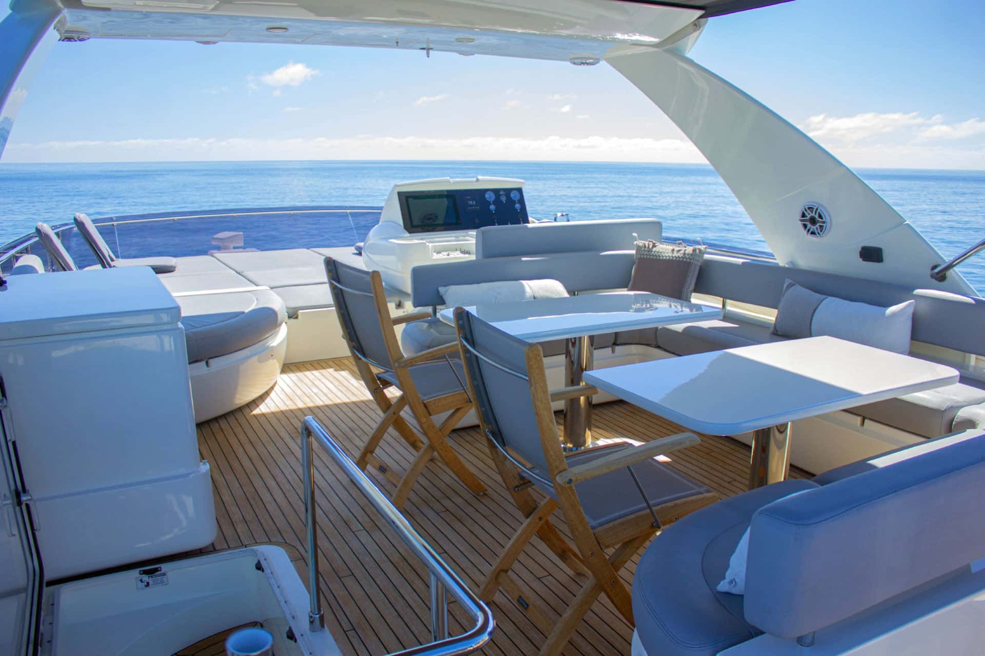 Flybridge with two white tables, teak folding chairs, a curved sofa and the upper helm