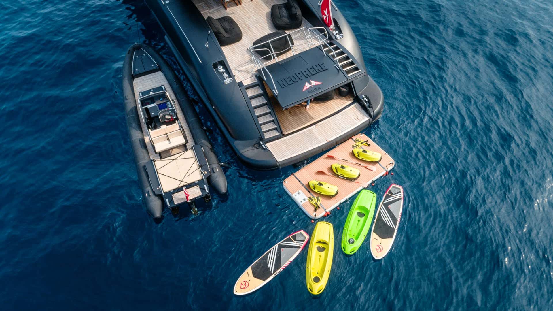 Aerial view of the stern with a black chase tender alongside and Seabobs, kayaks and paddleboards on a floating dock