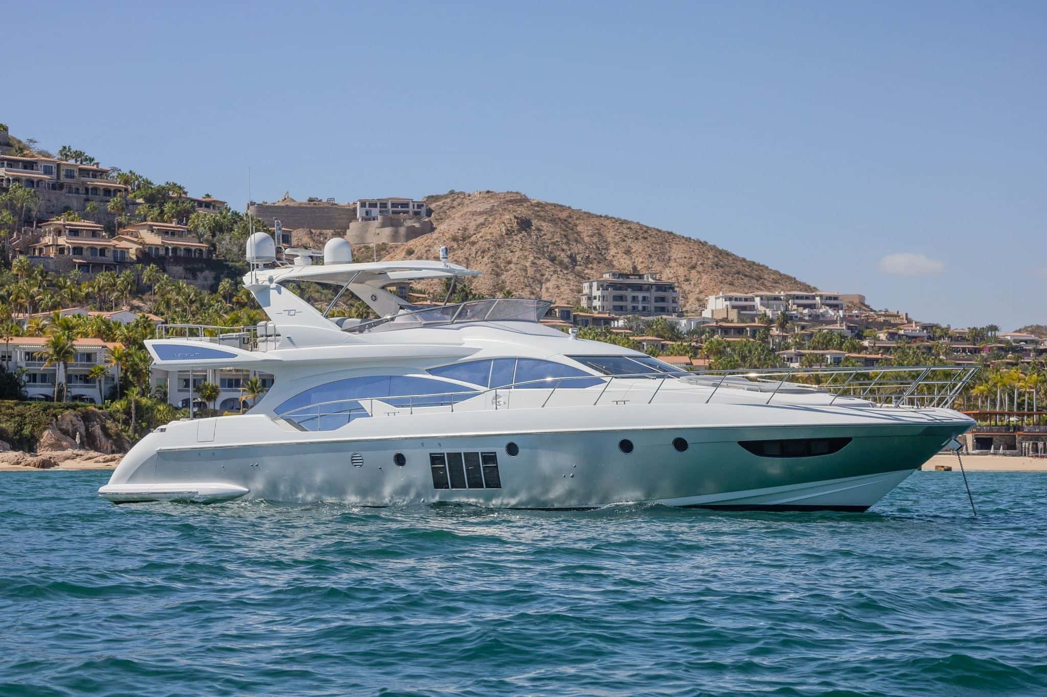 Side view of the white flybridge yacht at anchor below a hillside of villas near San José del Cabo