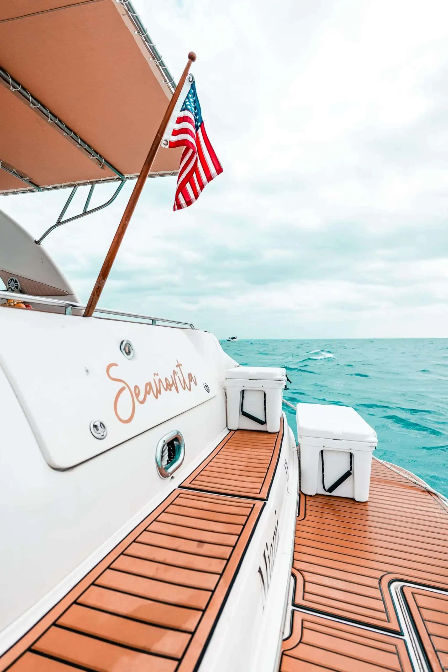 Aft deck of Seañorita with the name on the transom seat back, coolers and a flag