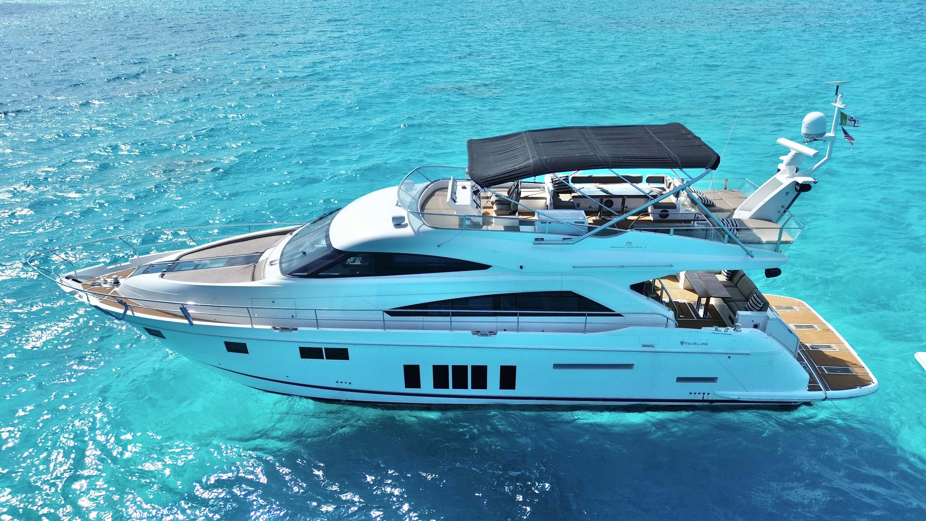 Aerial three-quarter view of Addicted from the bow, at anchor over turquoise water