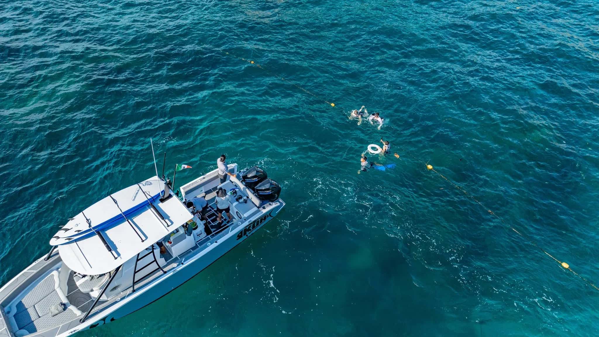 Aerial view of the boat on blue water with snorkellers swimming off its stern