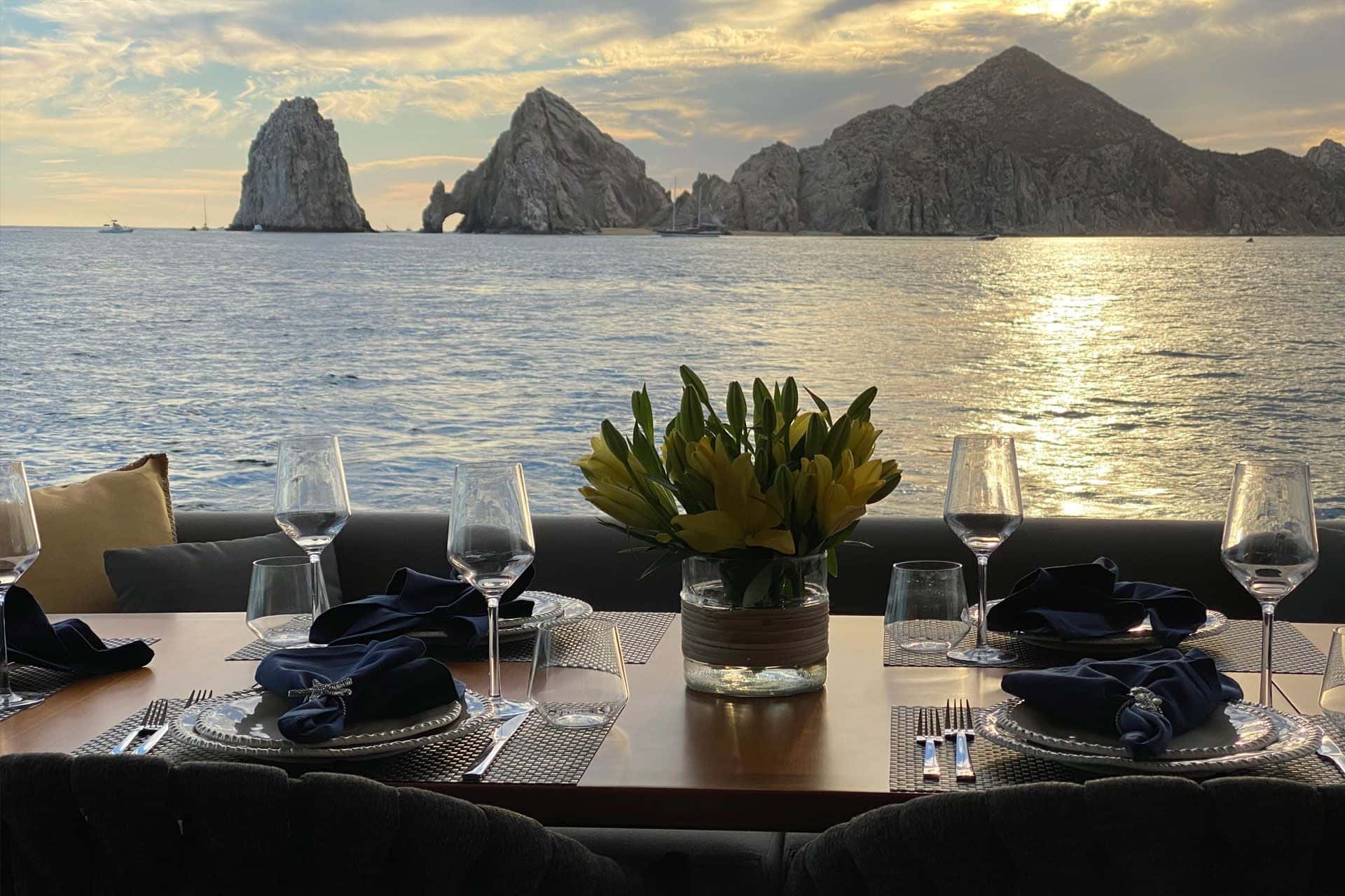 Wine glasses and navy napkins on a set table, the Land's End rocks at sunset beyond