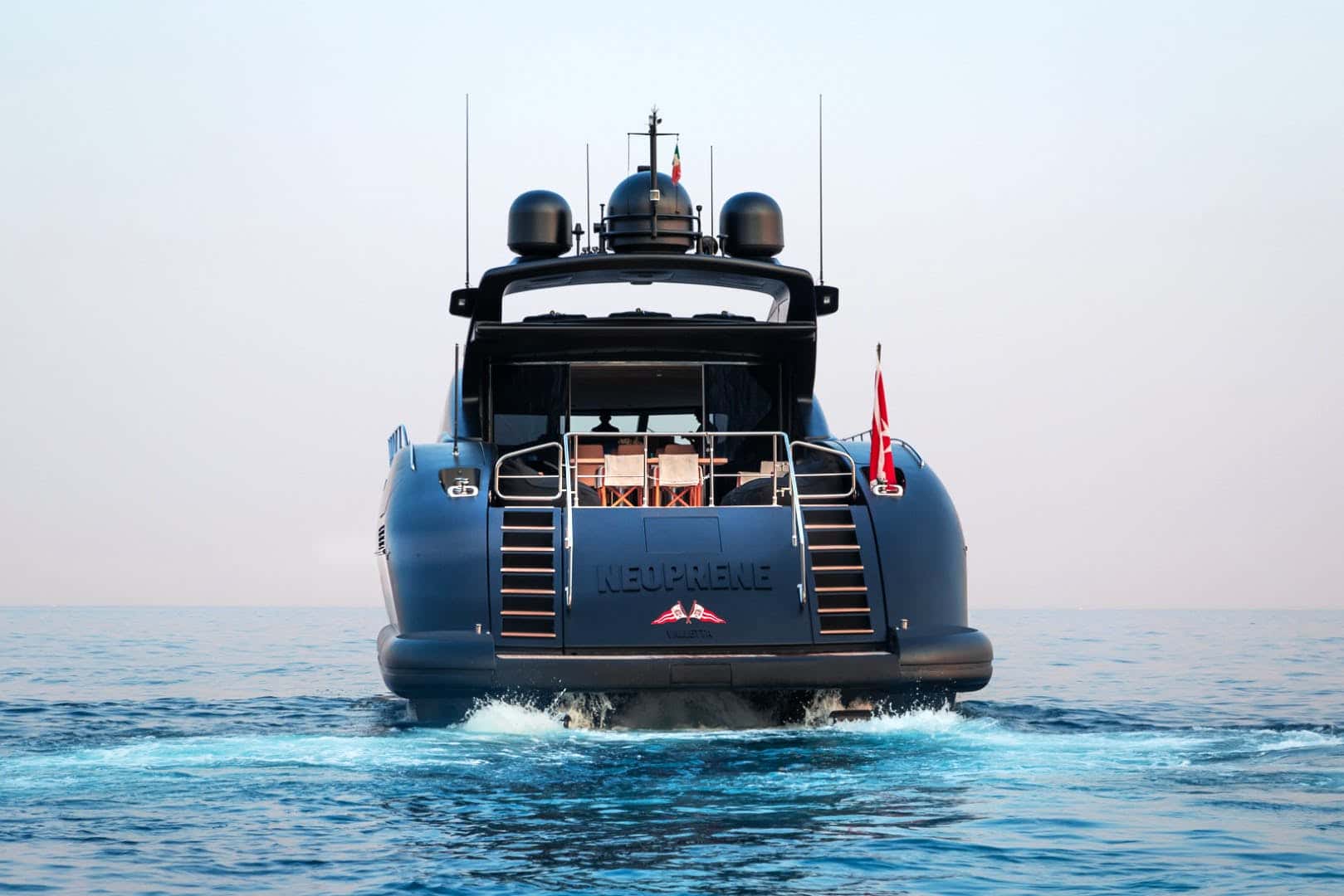 Stern of a matte black yacht lettered Neoprene, Valletta, with teak steps either side