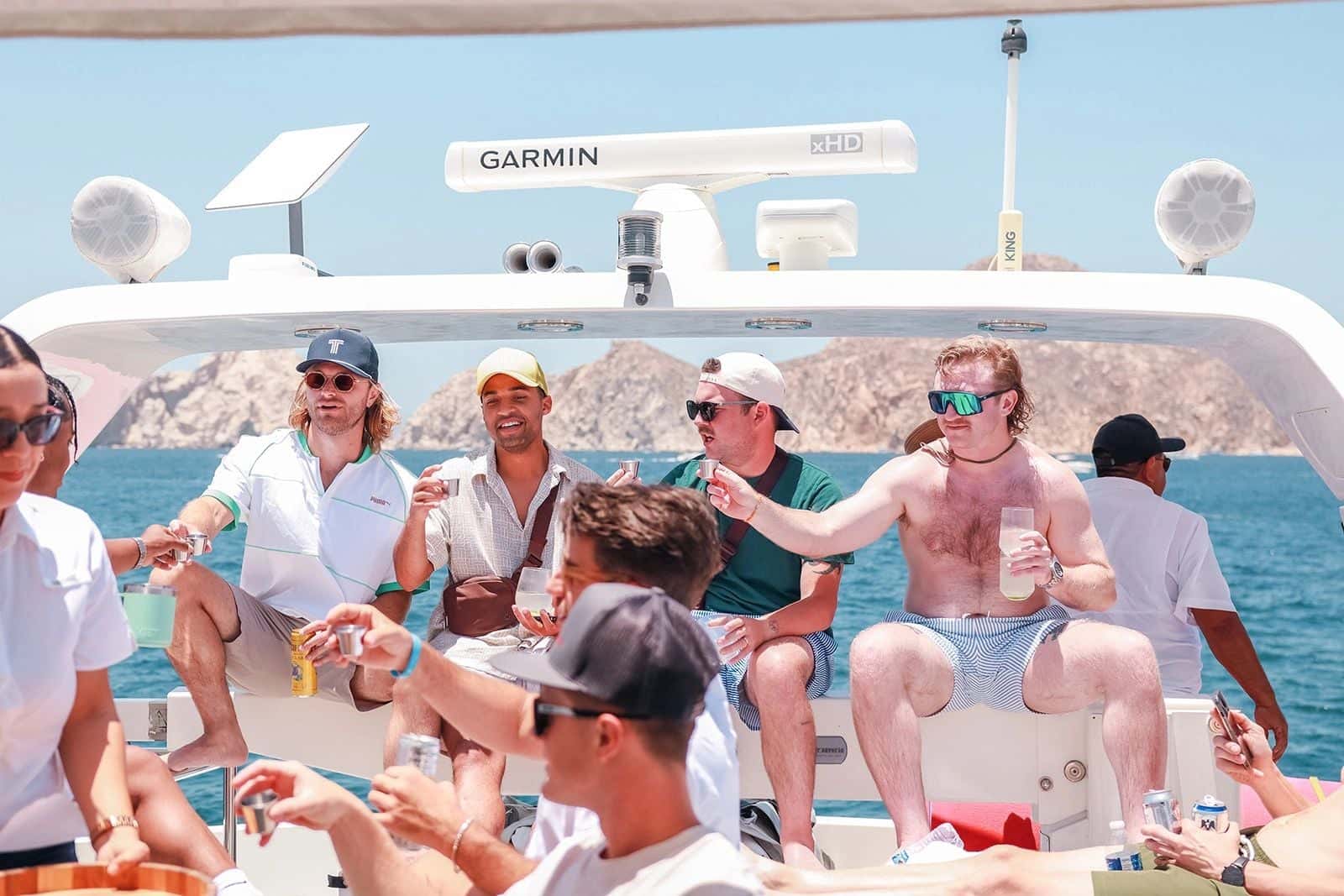 Guests raising drinks together on the flybridge, the bay behind