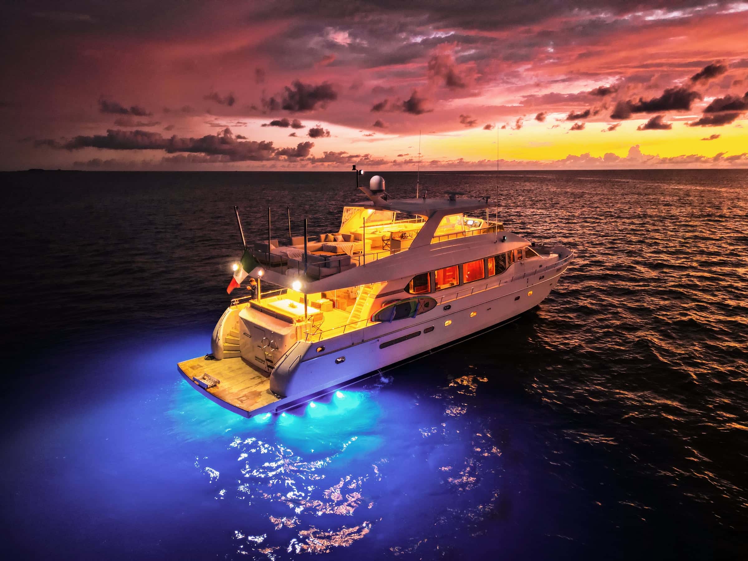 Yacht at dusk with lit decks and blue underwater lights at the stern