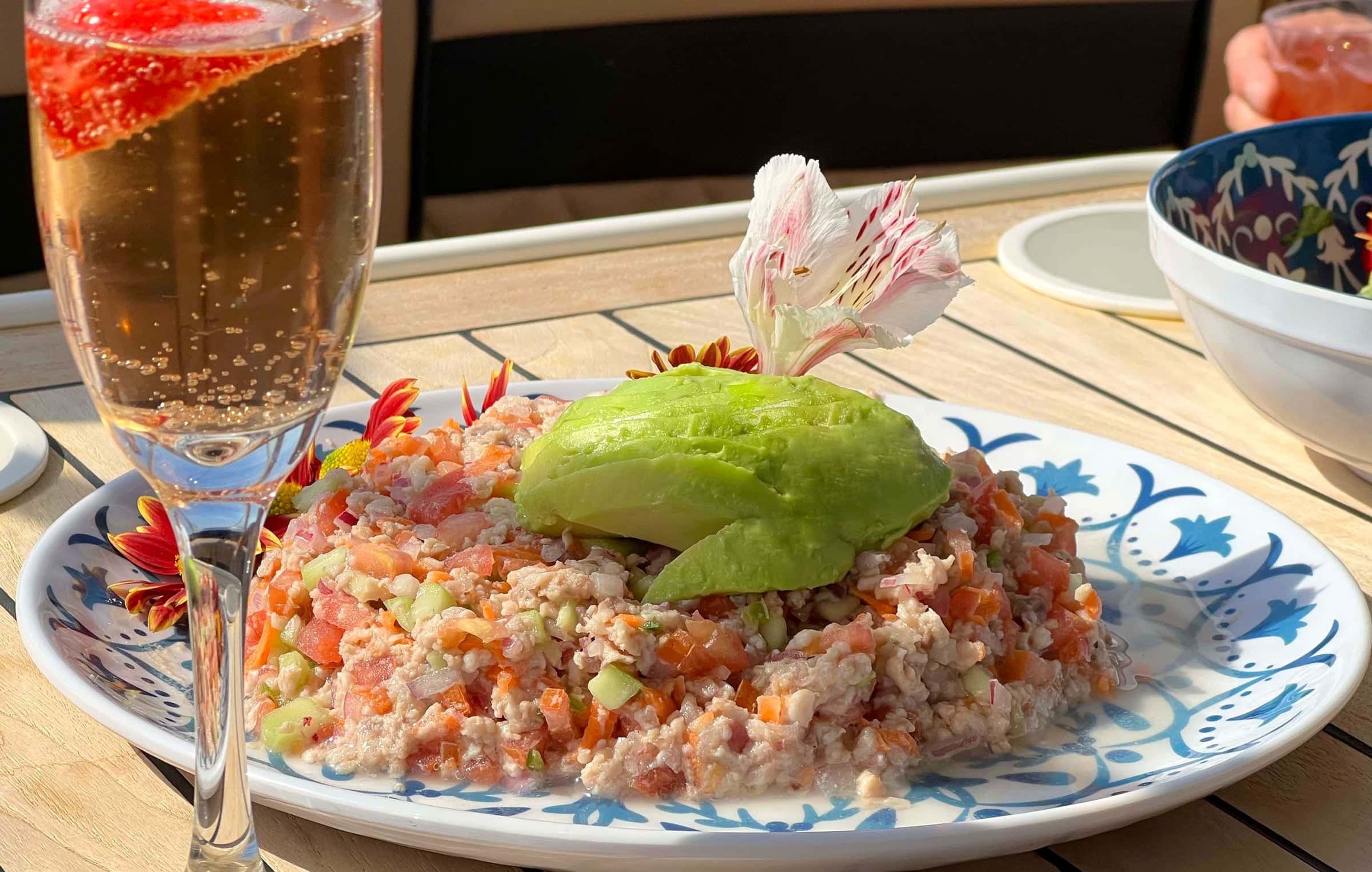 Glass of sparkling wine with a strawberry beside a plate of ceviche topped with avocado