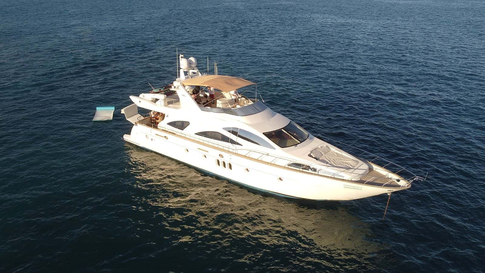 Aerial view of the white yacht at anchor in deep blue water, a float in the sea beside her