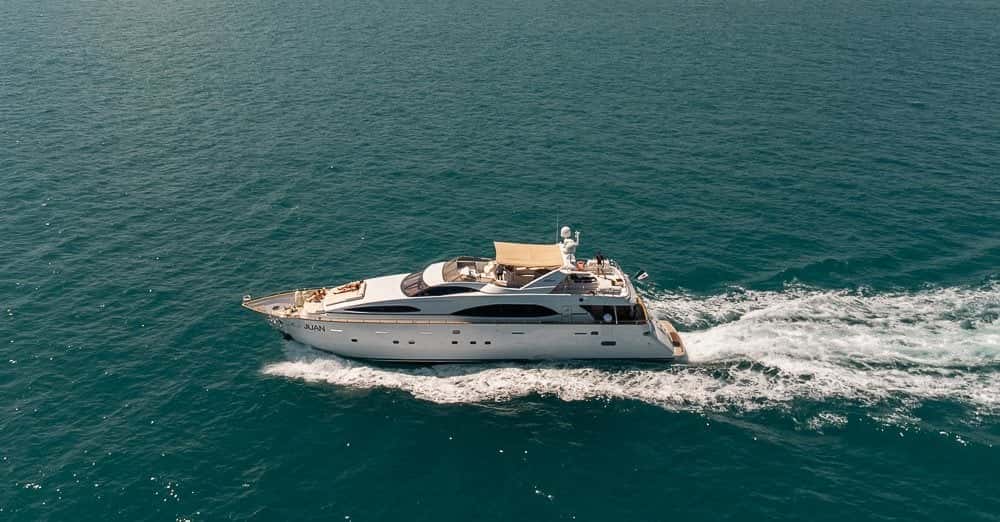 The white yacht under way on green-blue water, a long wake behind her