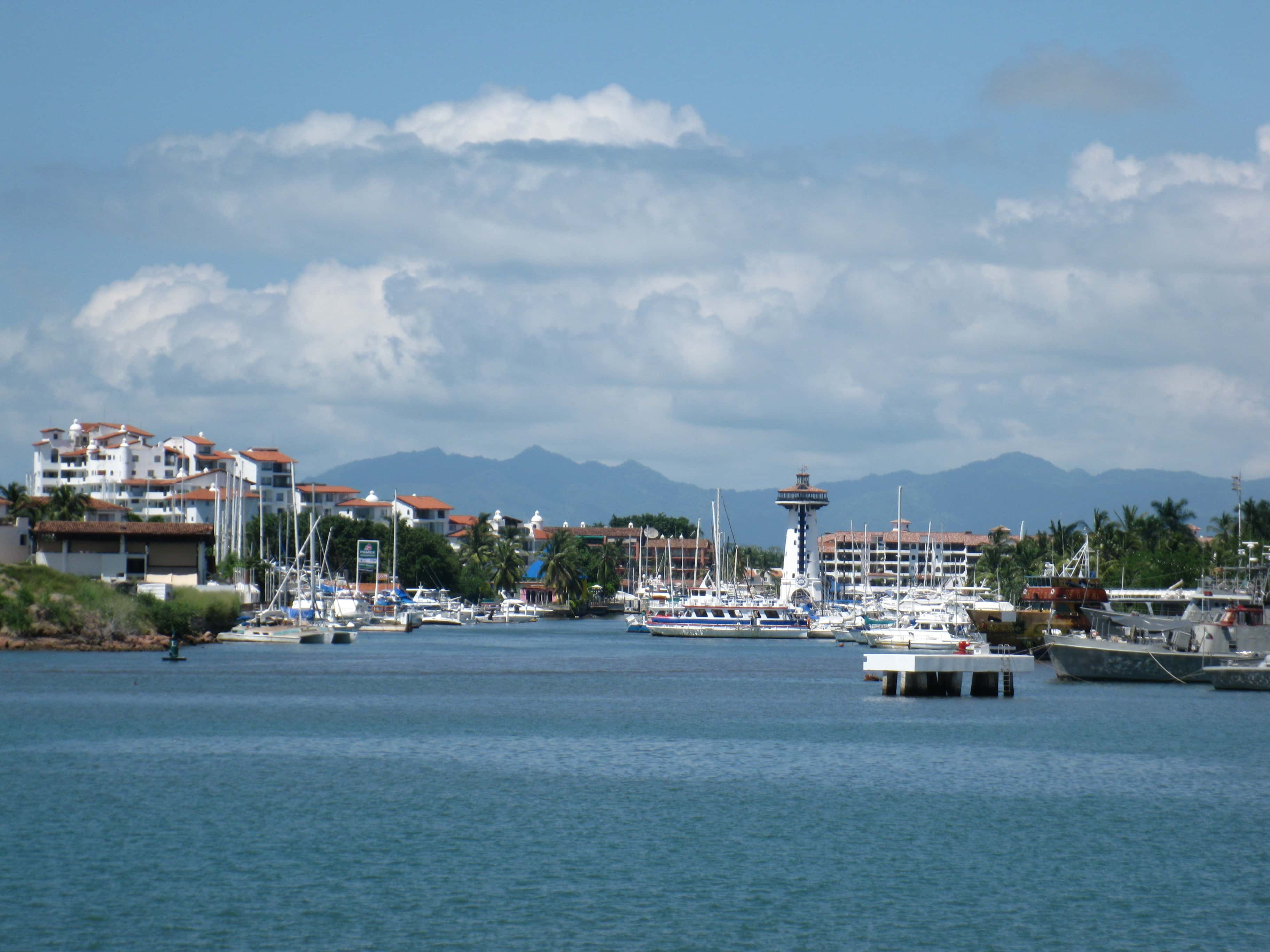 Marina Vallarta: the marina channel with moored boats, the white lighthouse tower and the hills behind