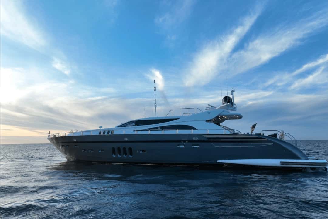 The yacht seen from the side under a blue sky at dusk, with a dark hull and white upper decks