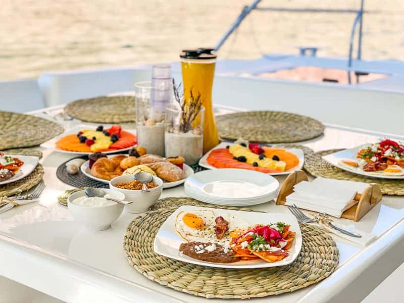 Breakfast table set on deck with eggs, chilaquiles, fruit plates, pastries and orange juice