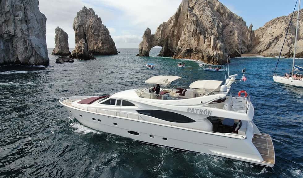 Patrón cruising past the rock arch, crew on the flybridge and a teak swim platform at the stern