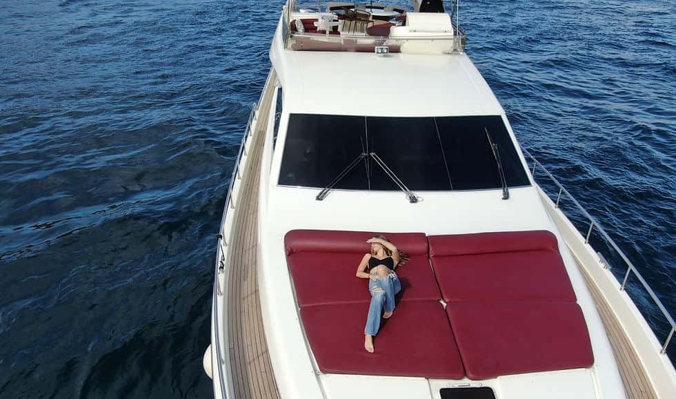 Woman lying on the red cushioned sun pad on the bow, seen from above
