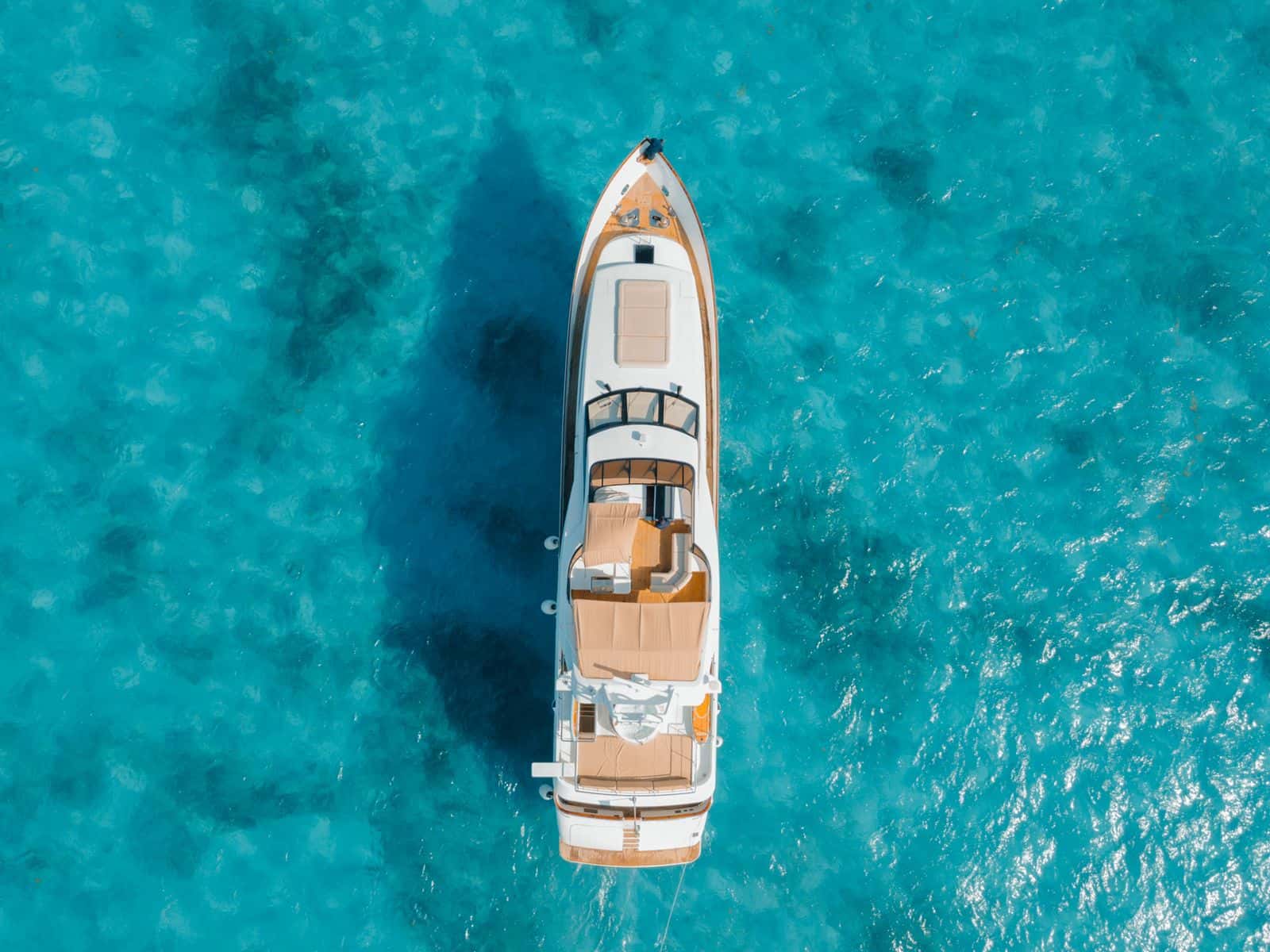 Aerial top-down view of the yacht at anchor on clear turquoise water, showing bow, flybridge and aft sunpads