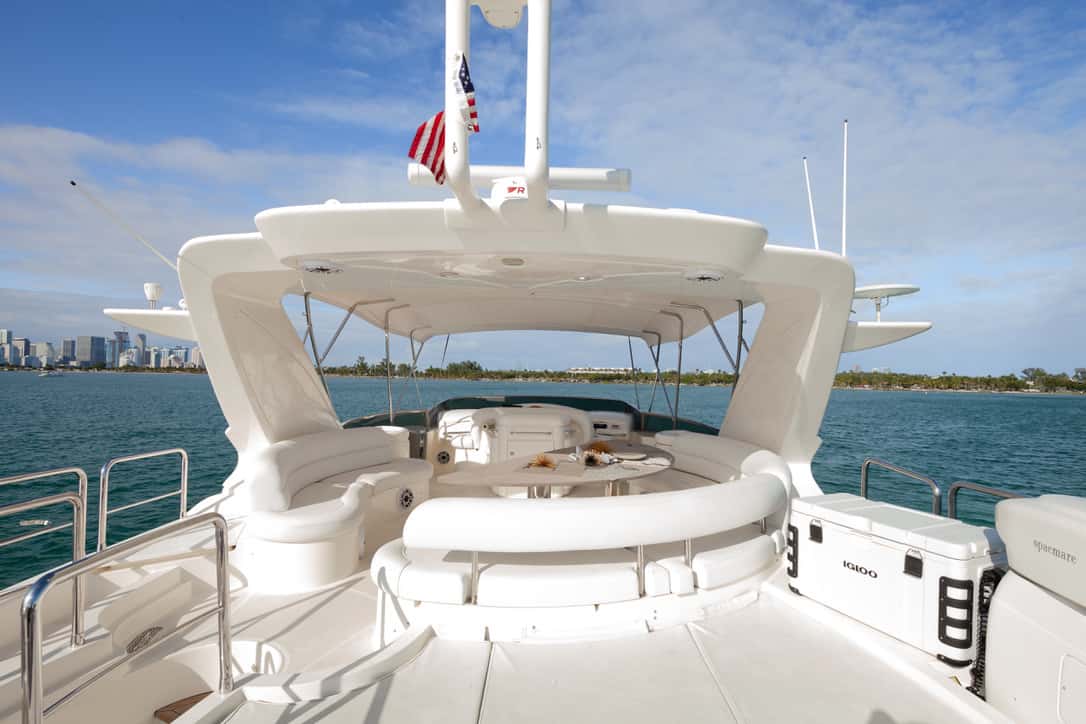 Flybridge with curved white seating, a central table, a hardtop and a cooler, the city skyline across the water