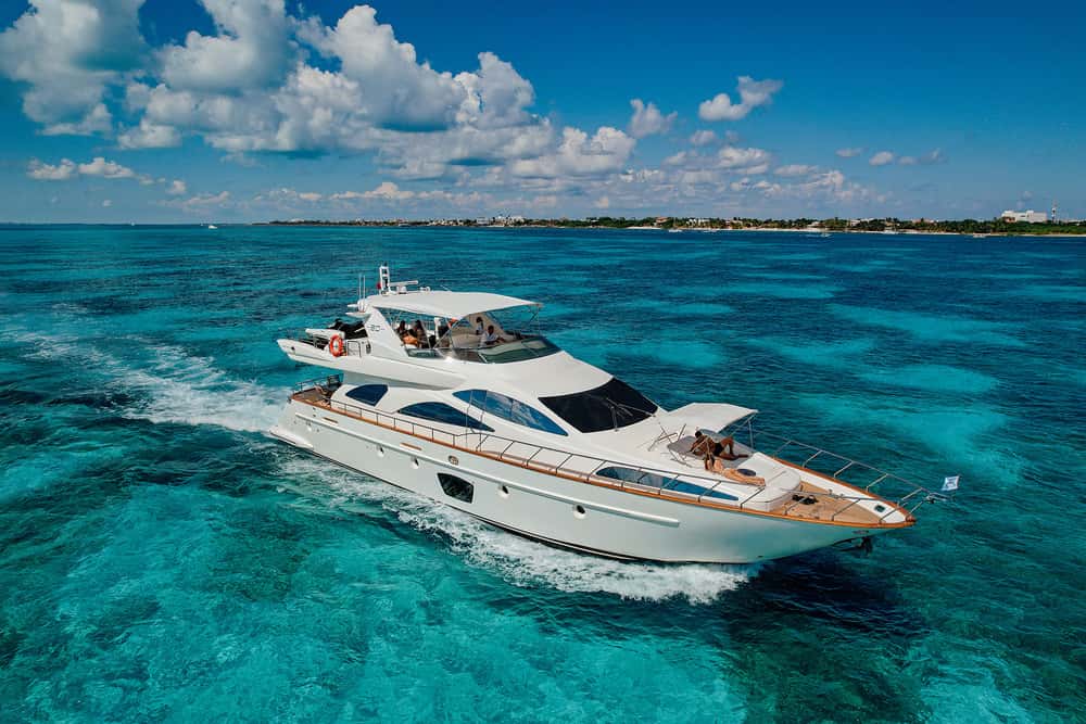 Aerial view of the yacht cruising over turquoise shallows with guests on the bow and flybridge
