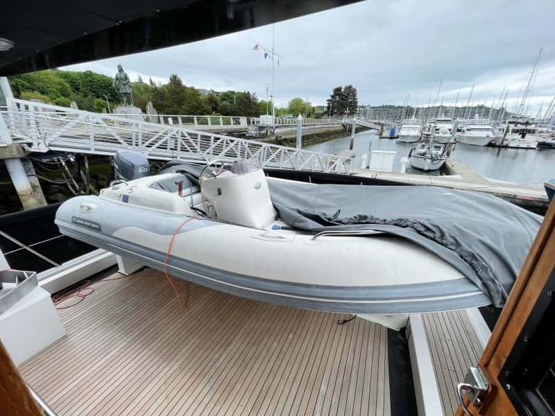 Inflatable tender with outboard motor under a grey cover on the teak aft deck beside a marina