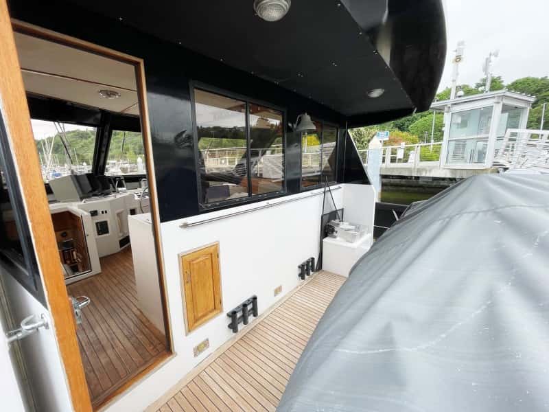 Teak side deck beside the pilothouse door with rod holders and a covered tender