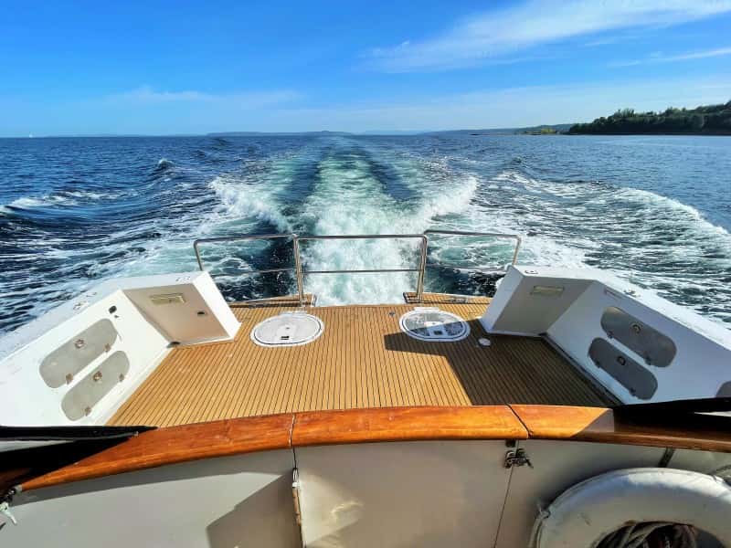 Teak aft deck with railing seen over the boat's churning wake