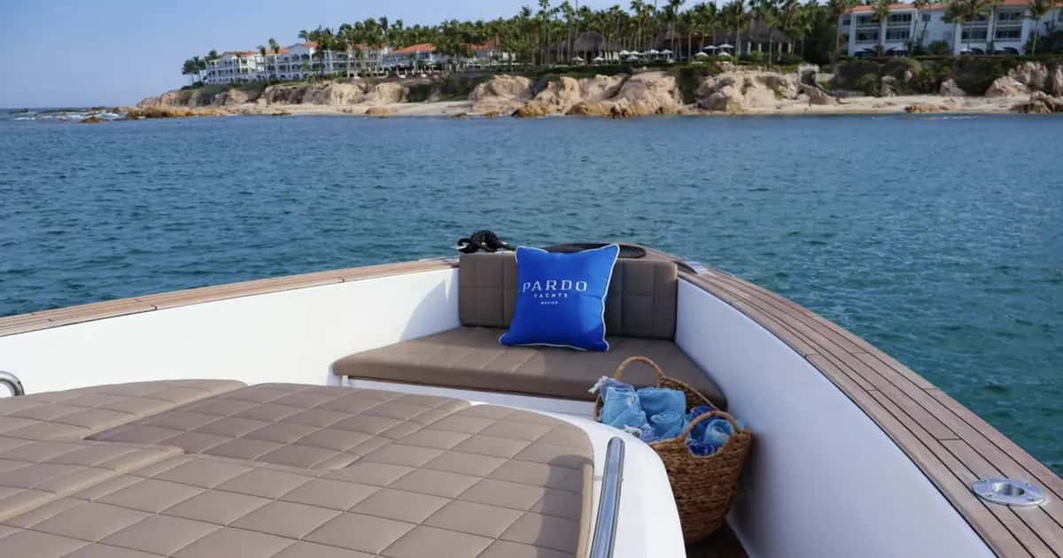 Bow seating with tan cushions, a blue Pardo Yachts pillow and a basket of towels, resort shoreline beyond