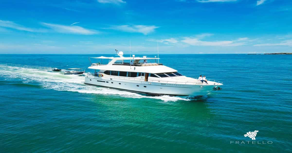 Yacht cruising on bright blue water with two guests sitting on the bow