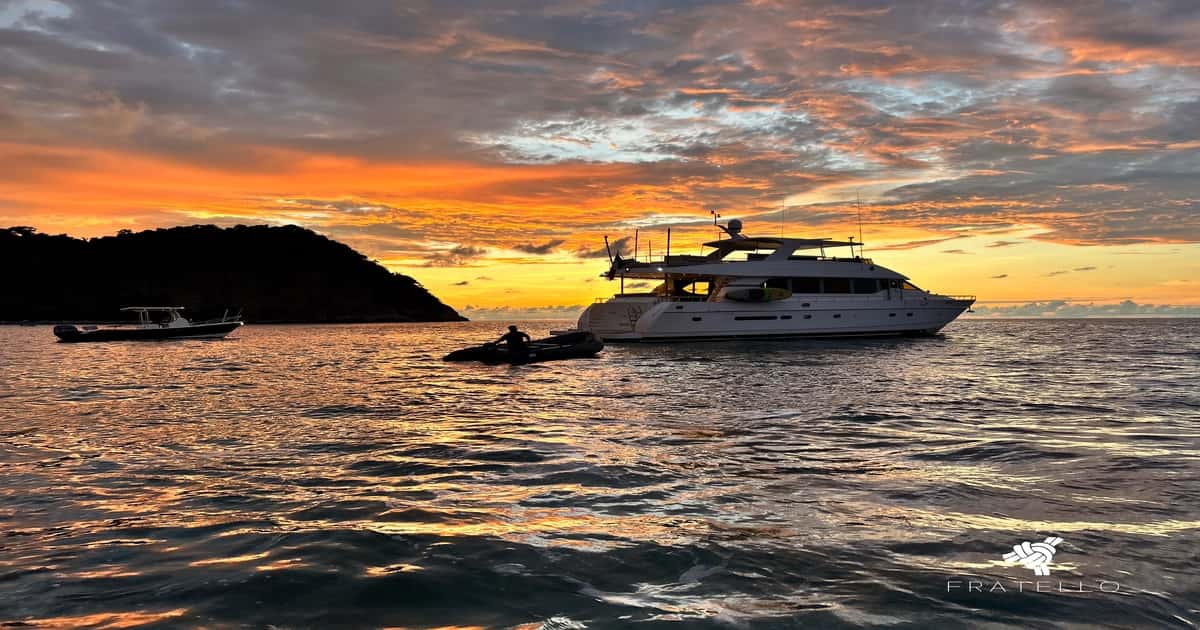 Yacht at anchor at sunset with a tender alongside and a hillside behind