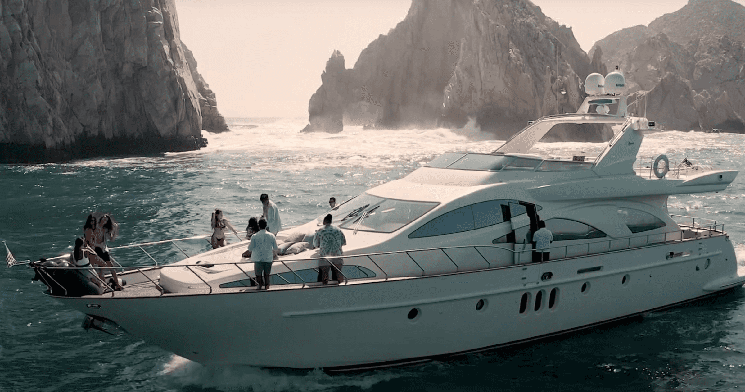 Heather Nikki, a white Azimut yacht, cruising past the rock arches at Land's End with guests on the bow