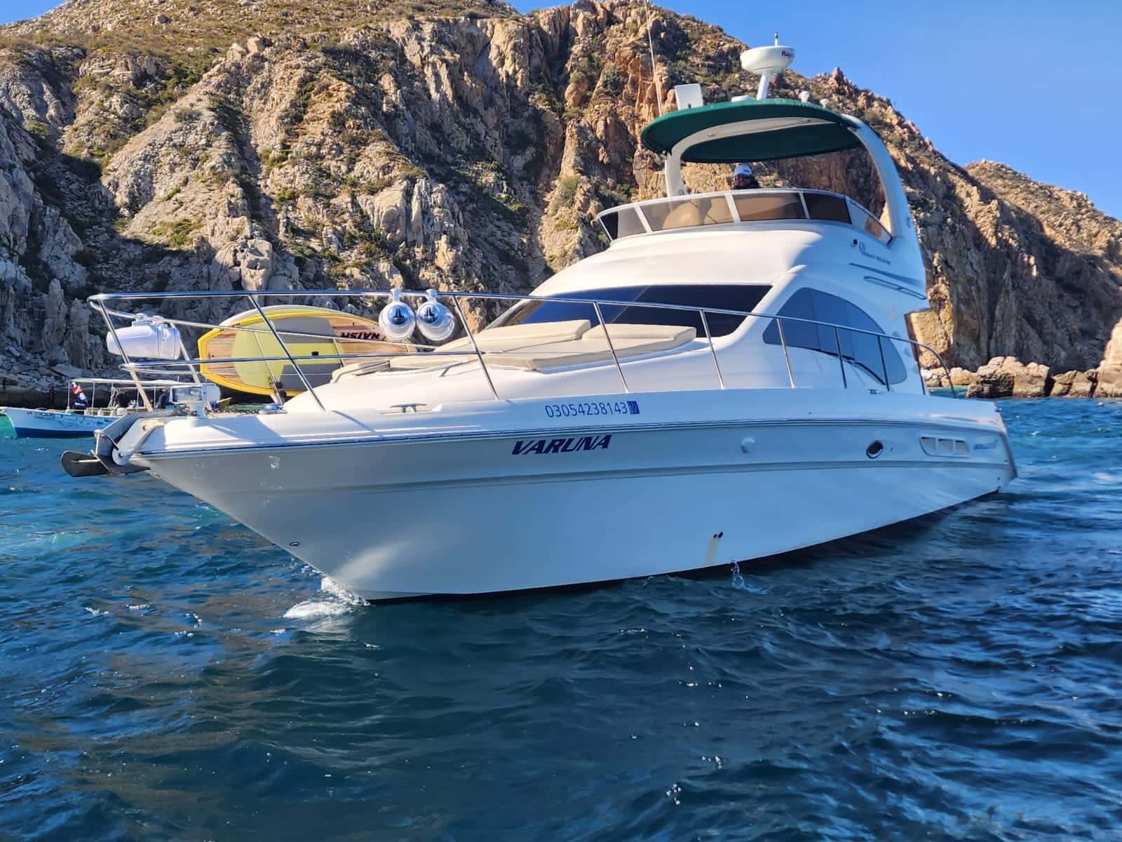 Vaduna, a white flybridge motor yacht anchored below rocky cliffs, paddle board on the bow