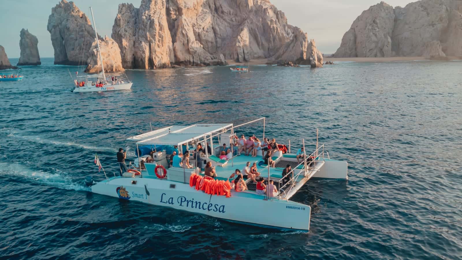 Catamaran with guests aboard, cruising in front of the rock formations at Land's End, Cabo