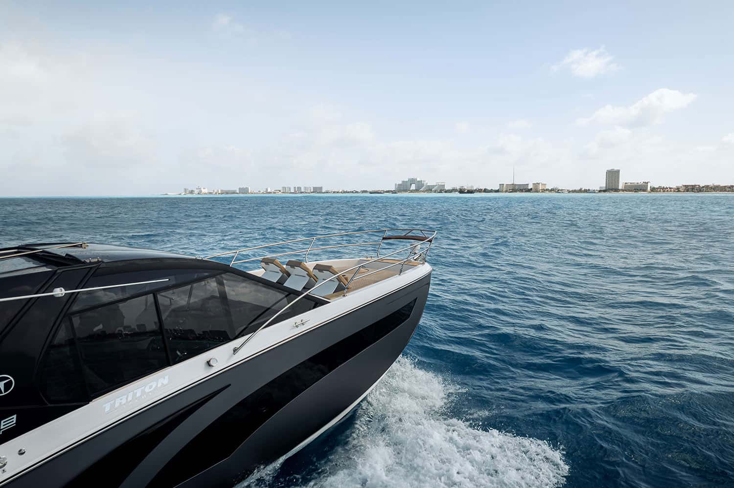 Bow of a dark-hulled yacht with sun pads and rails, a hotel skyline on the horizon