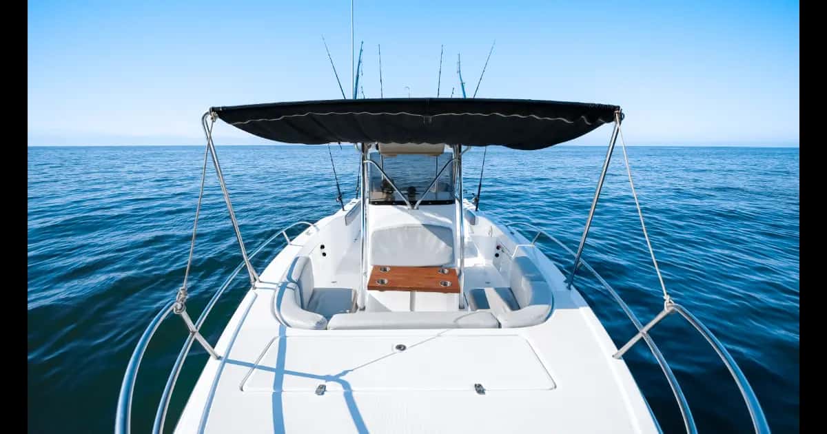 Bow seating under a black bimini, wrap-around cushions, teak table and open sea ahead