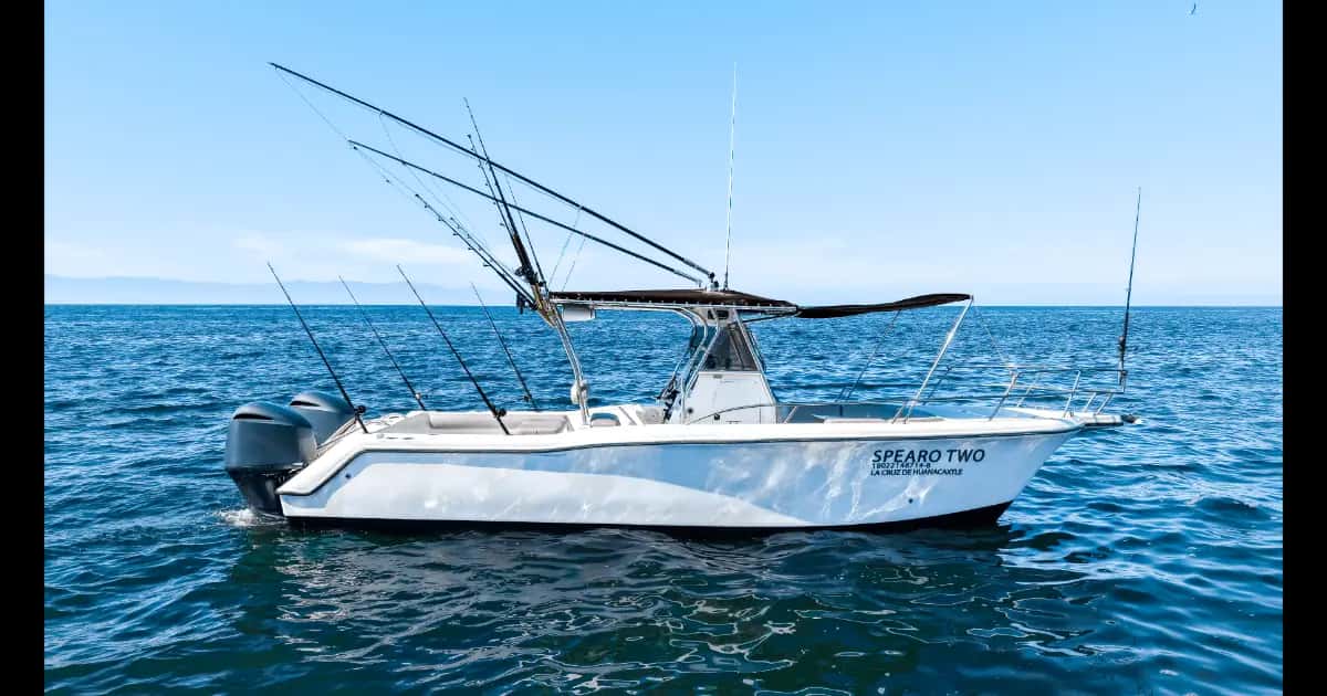 Spearo Two from the side at anchor, white hull, T-top with rods and twin outboard engines