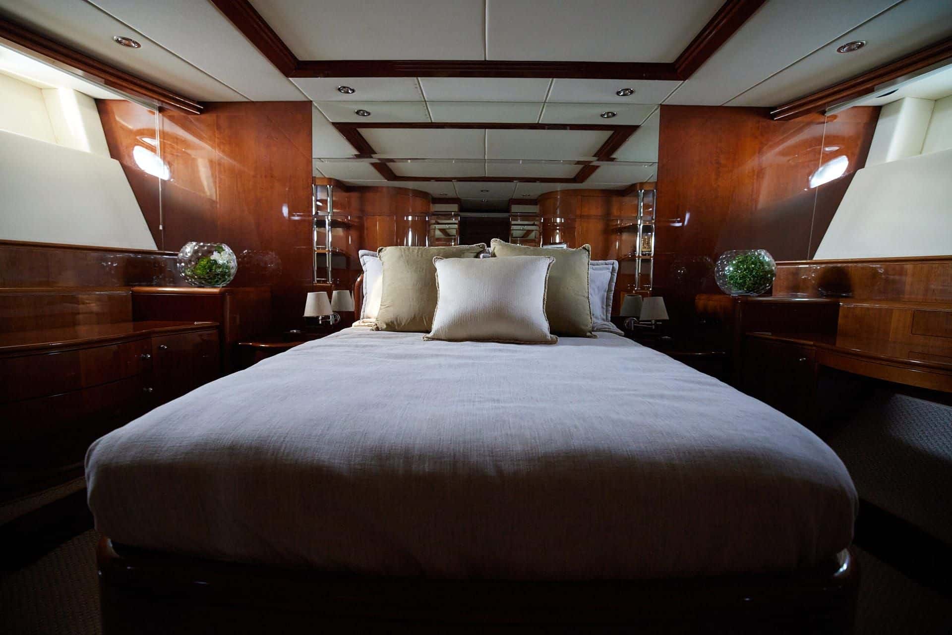 Master stateroom with a wide bed on a wood base between built-in counters and portholes