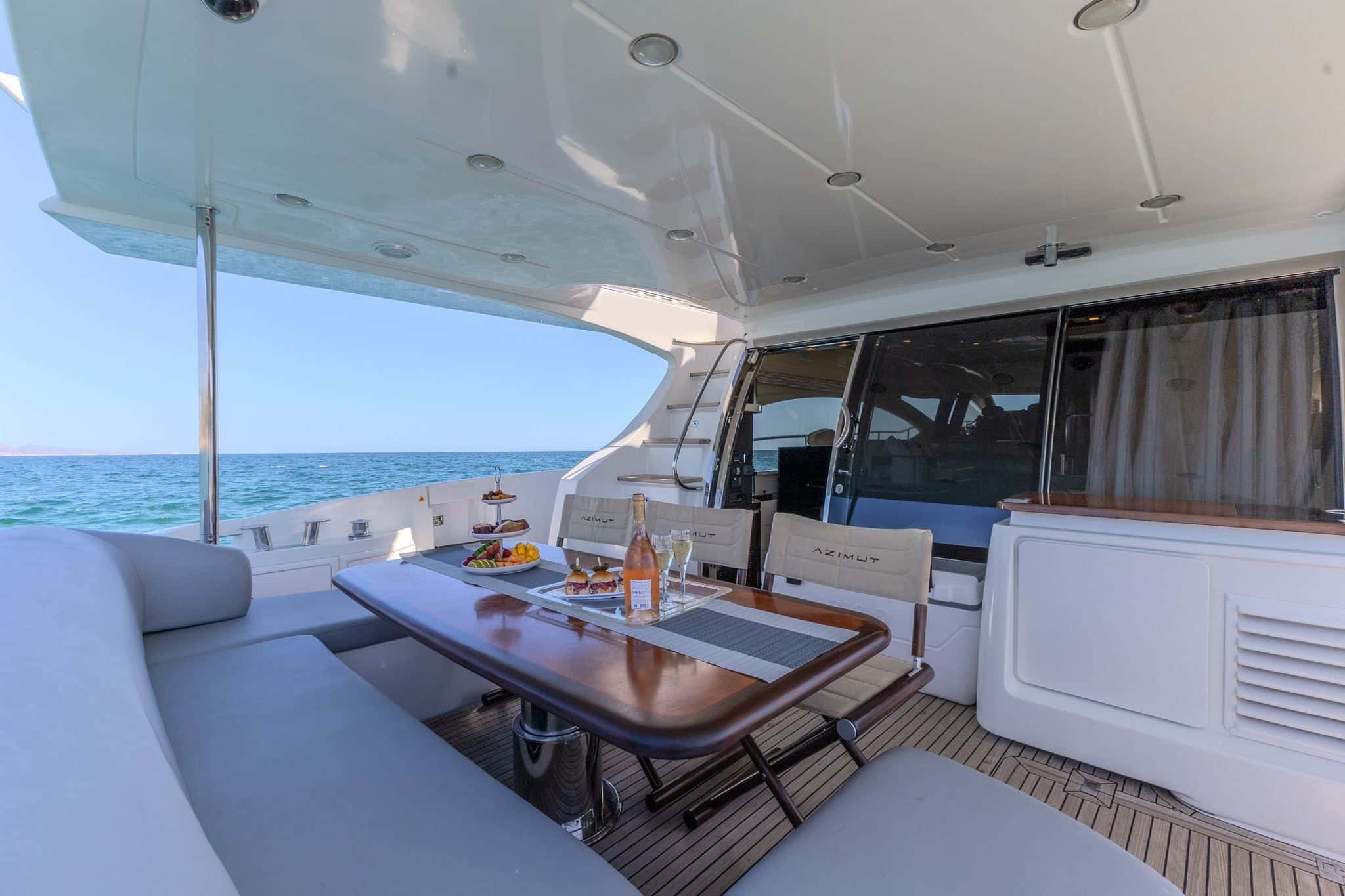 Covered aft deck with a cushioned bench around a wooden table on a teak floor