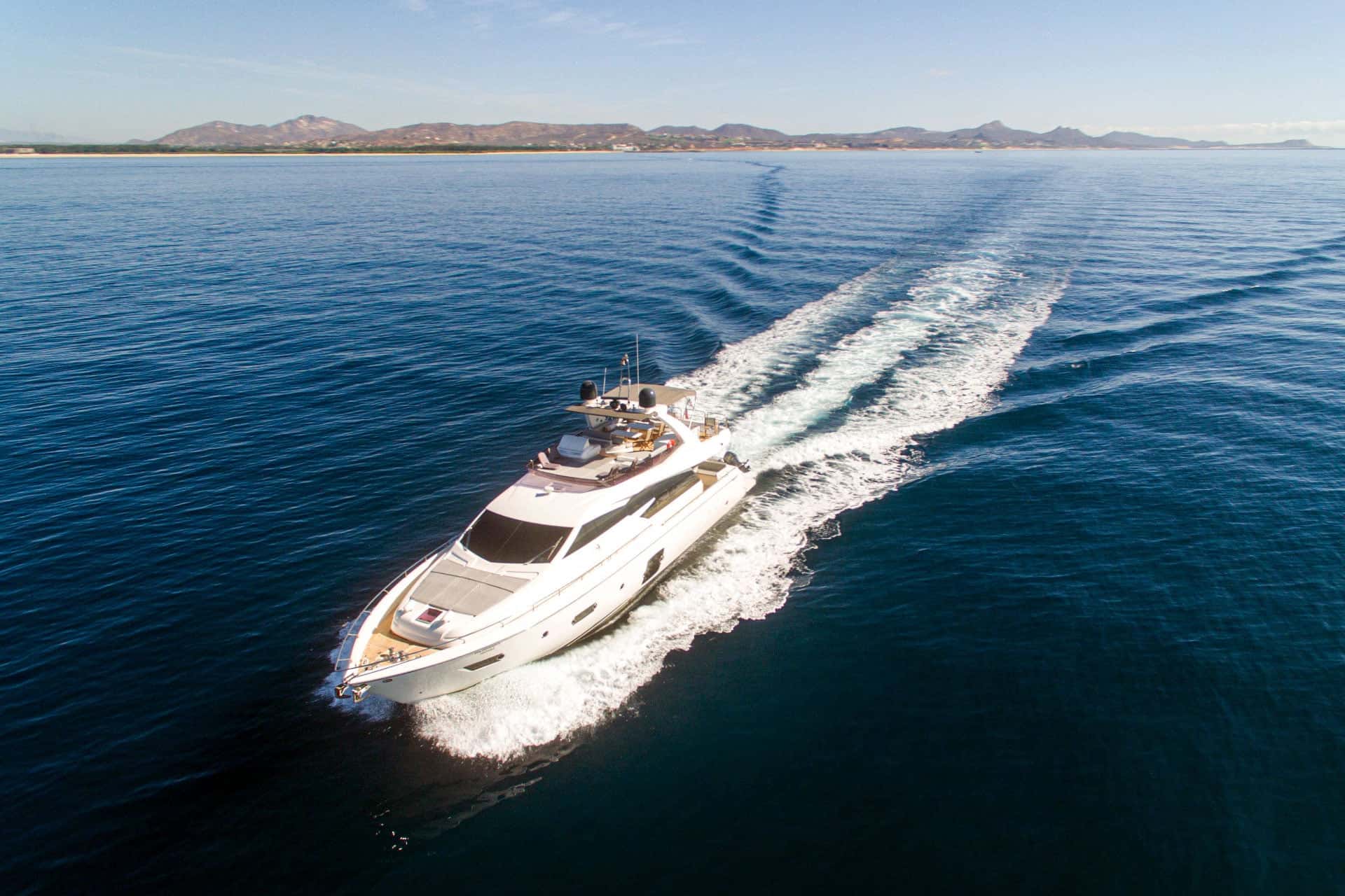 The yacht under way with a long white wake, the coast and hills behind