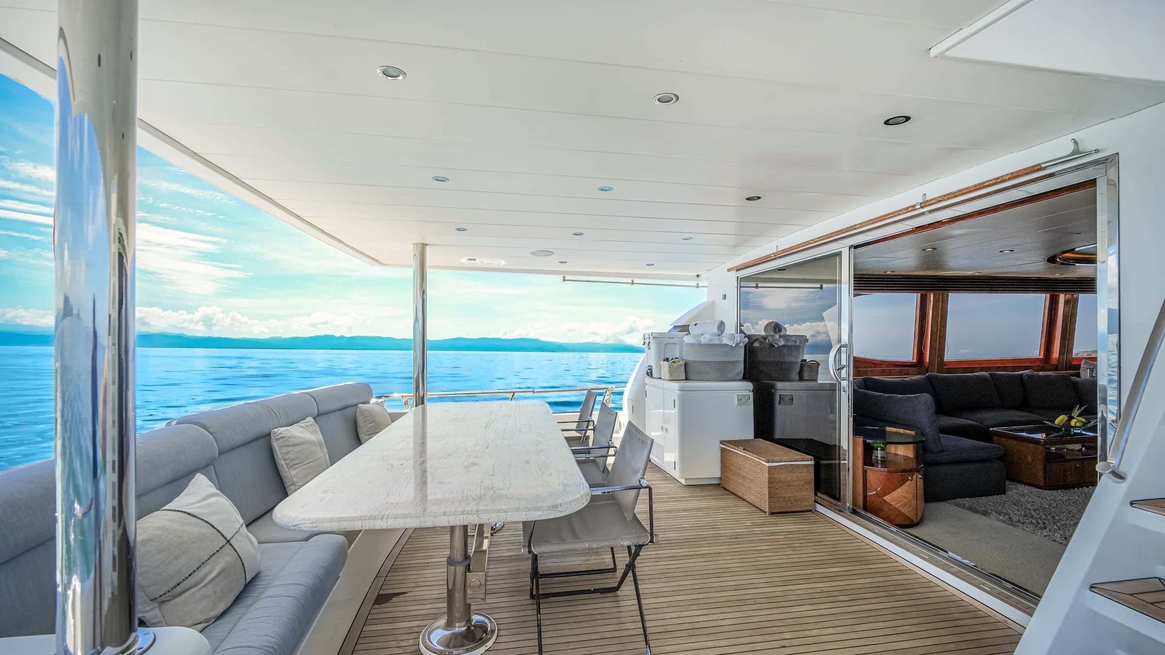 Covered aft deck with a stone dining table, cushioned bench and sliding doors to the saloon