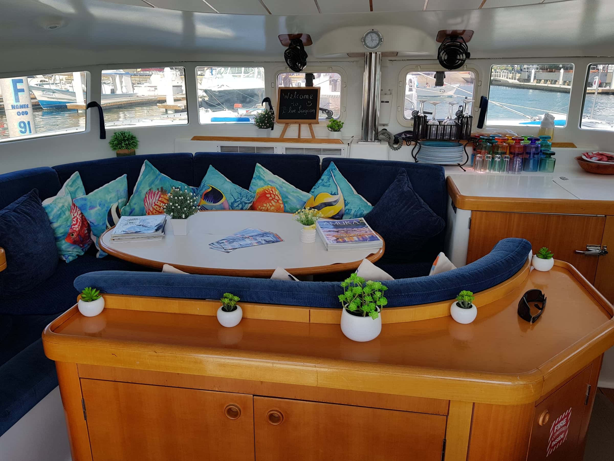 Saloon with a navy U-shaped settee, fish-print cushions and an oval table behind the galley counter