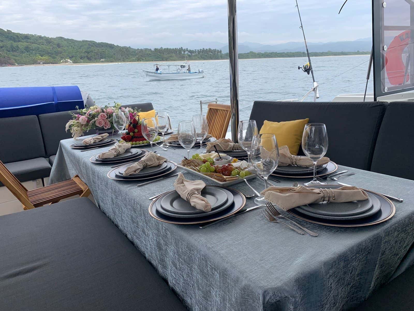 Cockpit table laid for dinner with grey plates, glasses and flowers, the bay beyond