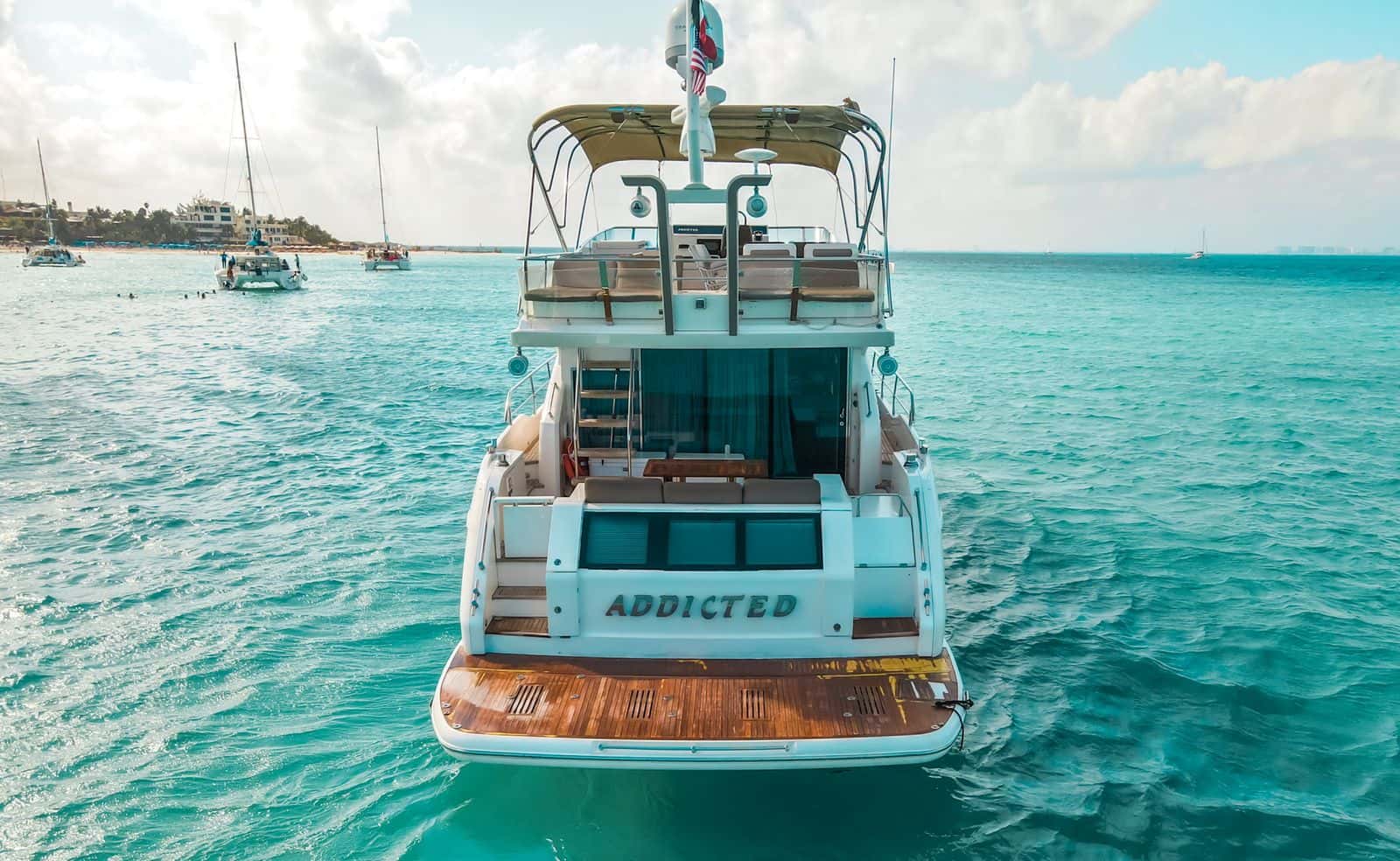 Addicted seen from astern at anchor off a beach, with the name on the transom and the flybridge above the cockpit