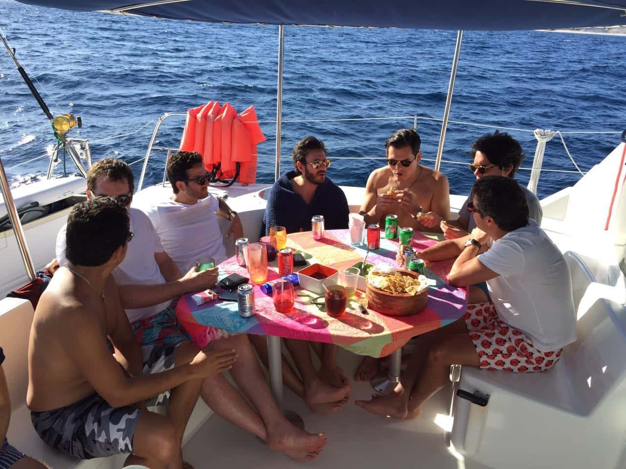 Guests at lunch around the cockpit table under the blue bimini, plates of chips and salsa